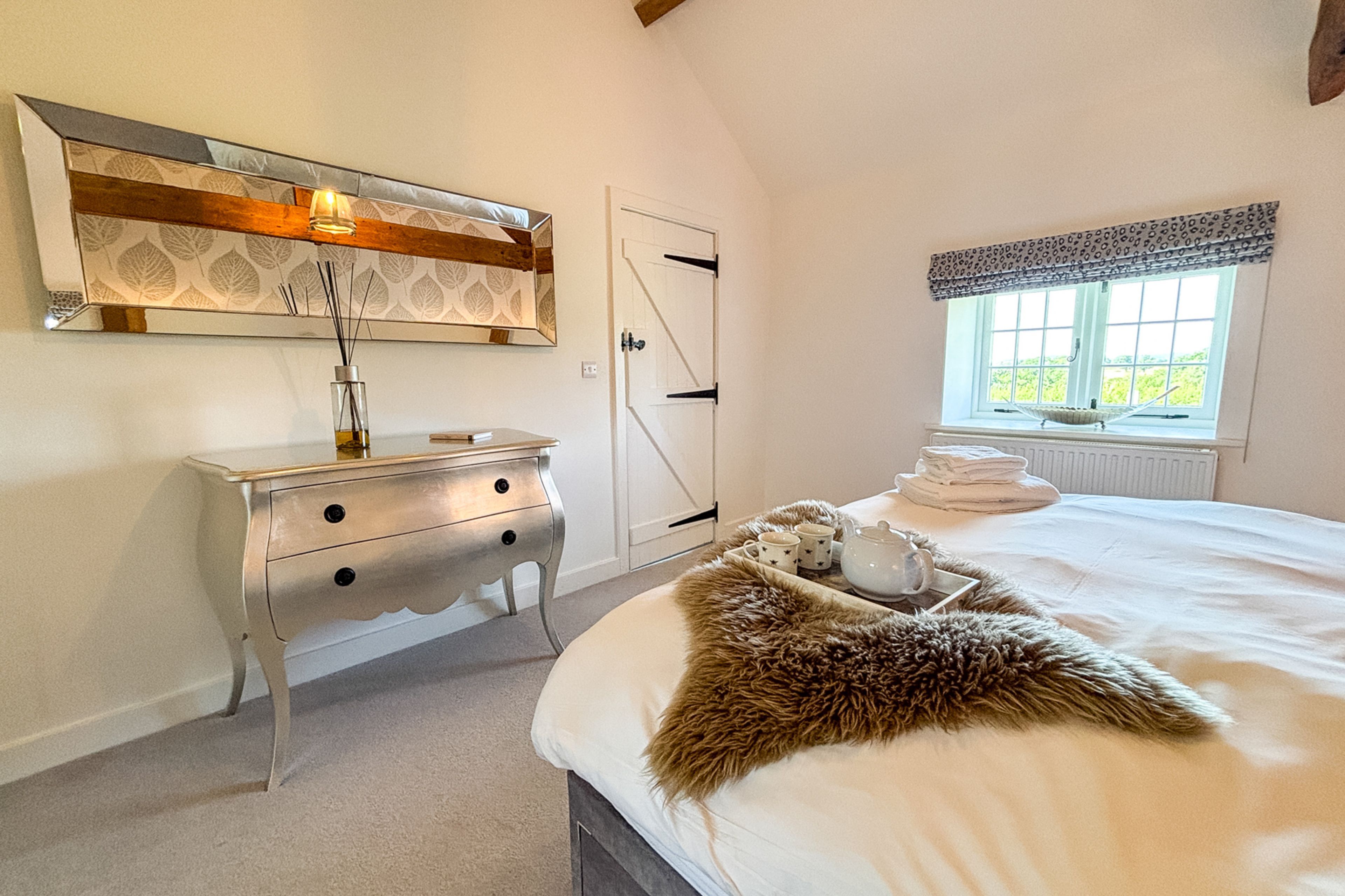 A bedroom with a bed, a dresser, a mirror, a window with a view, and a door.