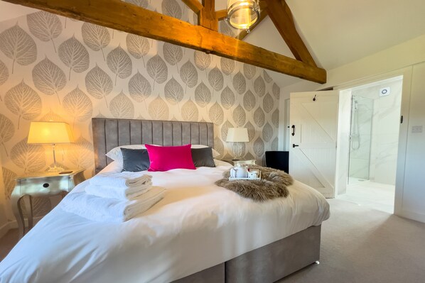 A bedroom with a bed, pillows, a nightstand, a lamp, a fluffy throw, and a door leading to a bathroom.