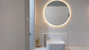A modern bathroom with a white sink, a round mirror with a light halo, and a small plant on the counter. - Namhae Seven House (Namhae)