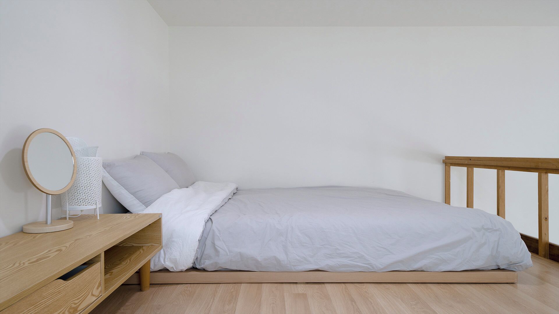A minimalist bedroom with a single bed, a wooden nightstand, a round mirror, and a white chair.