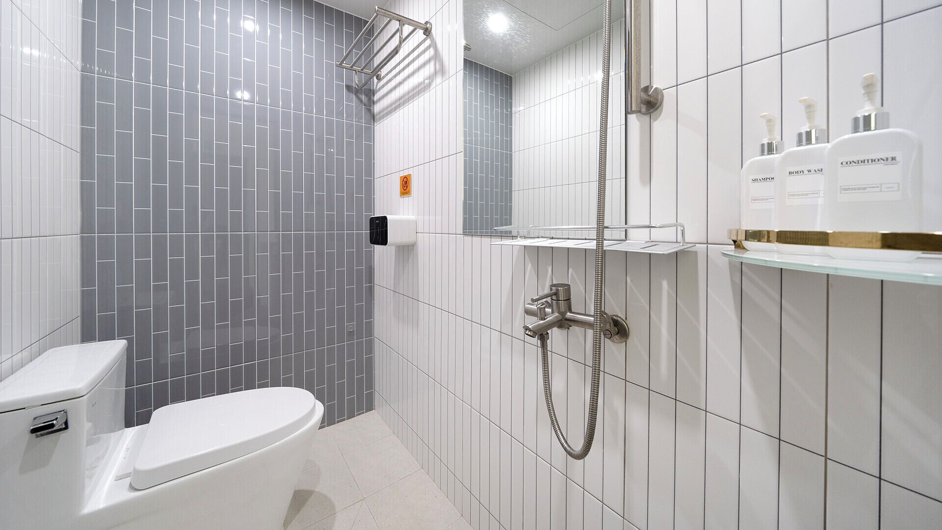 A modern bathroom with a toilet, a shower, and a shelf with toiletries.