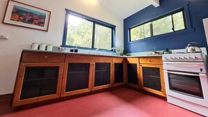 Une cuisine avec des meubles en bois, un fourneau blanc et deux fenêtres donnant sur un paysage verdoyant.