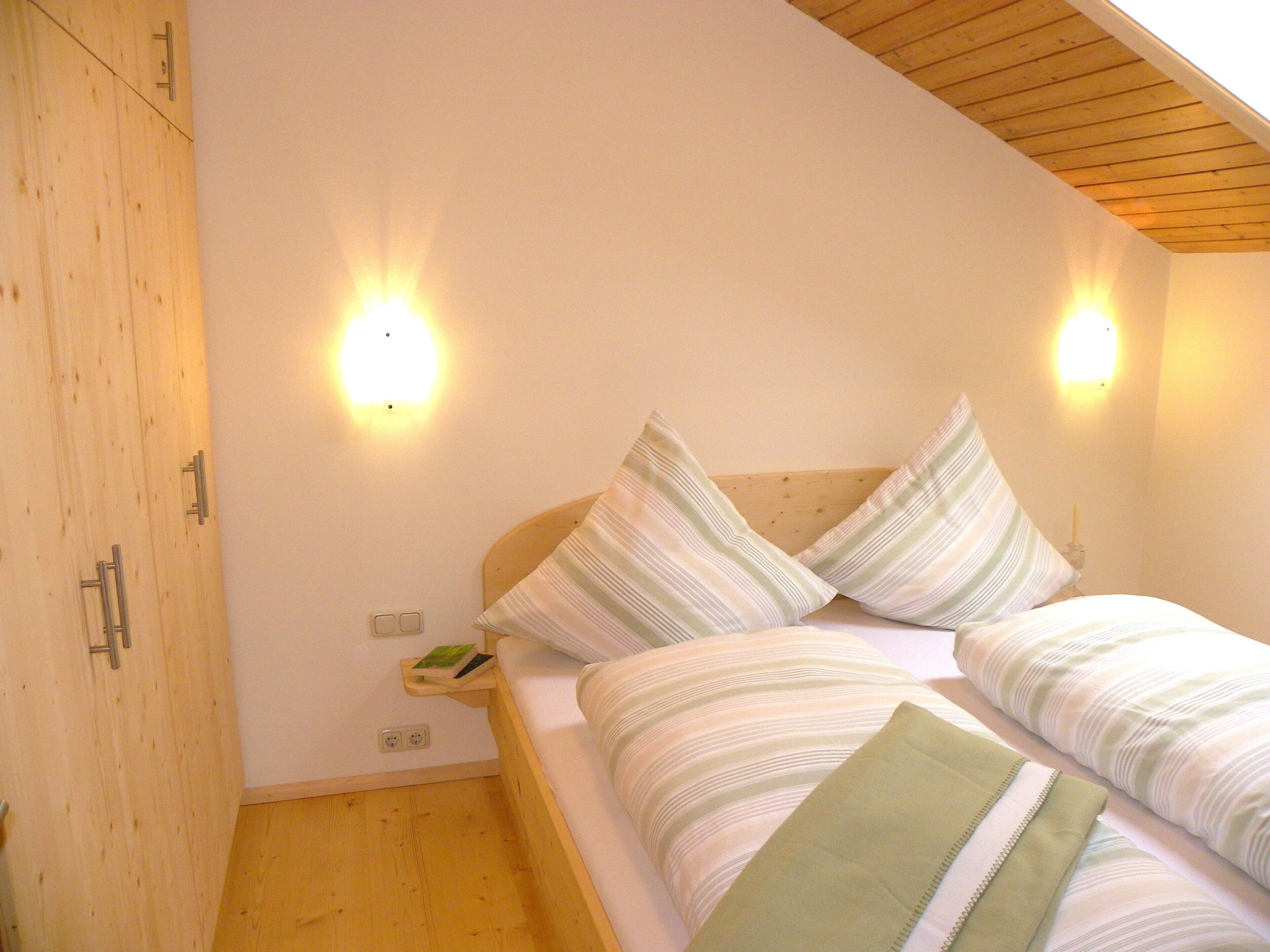 A bedroom with a wooden ceiling, two bedside lamps, a bed with striped bedding, and a bedside table with a book.
