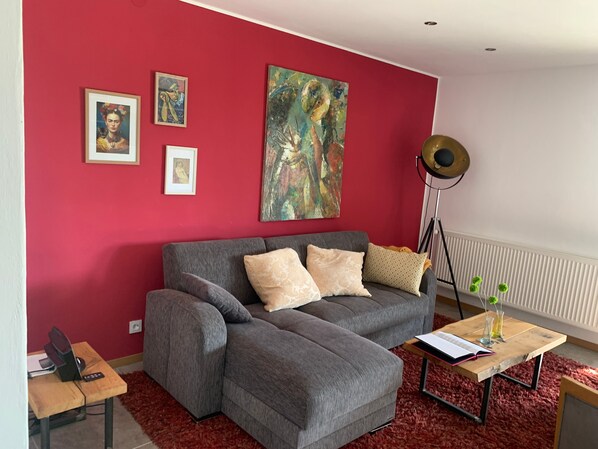Un salon moderne avec un canapé gris, des murs rouges et trois œuvres d’art encadrées.