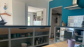 A modern kitchen with a wooden table, shelves with dishes, and a built-in oven. - Apartment "Draußen am See" with Private Sauna, Garden & Wi-Fi (Losheim)