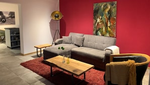 A modern living room with a grey sofa, a wooden coffee table, a red rug, a floor lamp, and a painting on the wall. - Apartment "Draußen am See" with Private Sauna, Garden & Wi-Fi (Losheim)