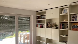 A room with a sliding glass door, a tiled floor, and a white shelving unit with books and decorative items. - Apartment "Draußen am See" with Private Sauna, Garden & Wi-Fi (Losheim)