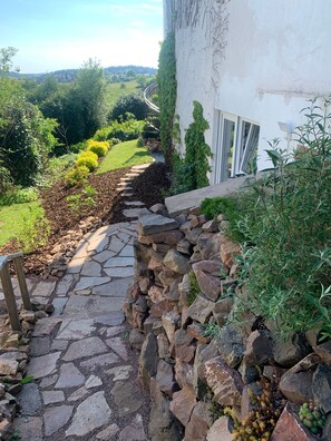 Un chemin de pierre mène à un bâtiment blanc qui offre une vue sur un jardin.