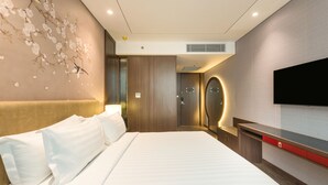 A hotel room with a large bed, a TV mounted on the wall, and a decorative wall with floral patterns. - Ashley Tang Menteng Jakarta (Jakarta)