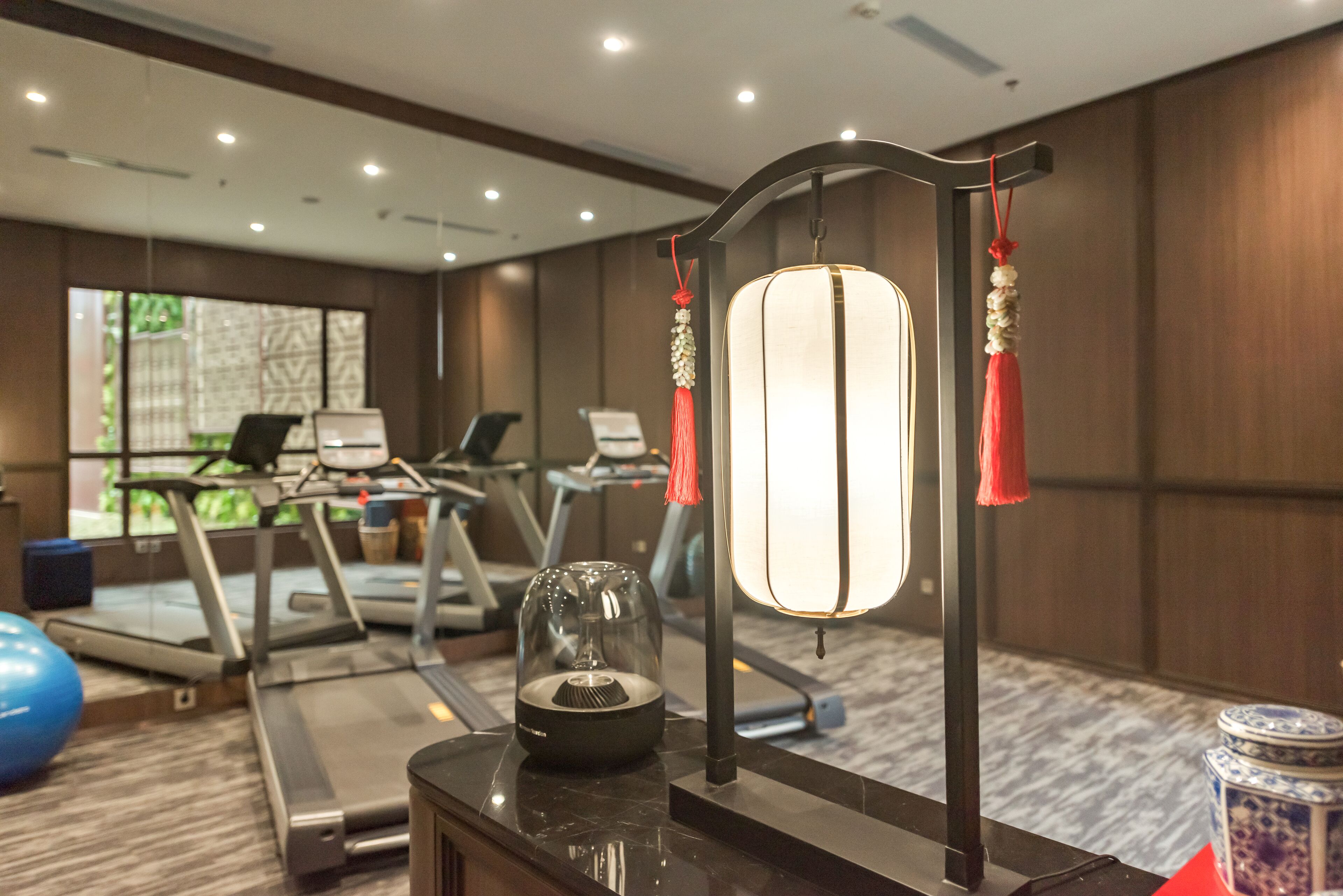A hotel room with exercise equipment, a decorative lamp, and a view of the outdoors.