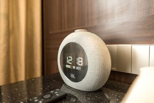 A JBL smart speaker on a countertop with a digital display showing the time and date.