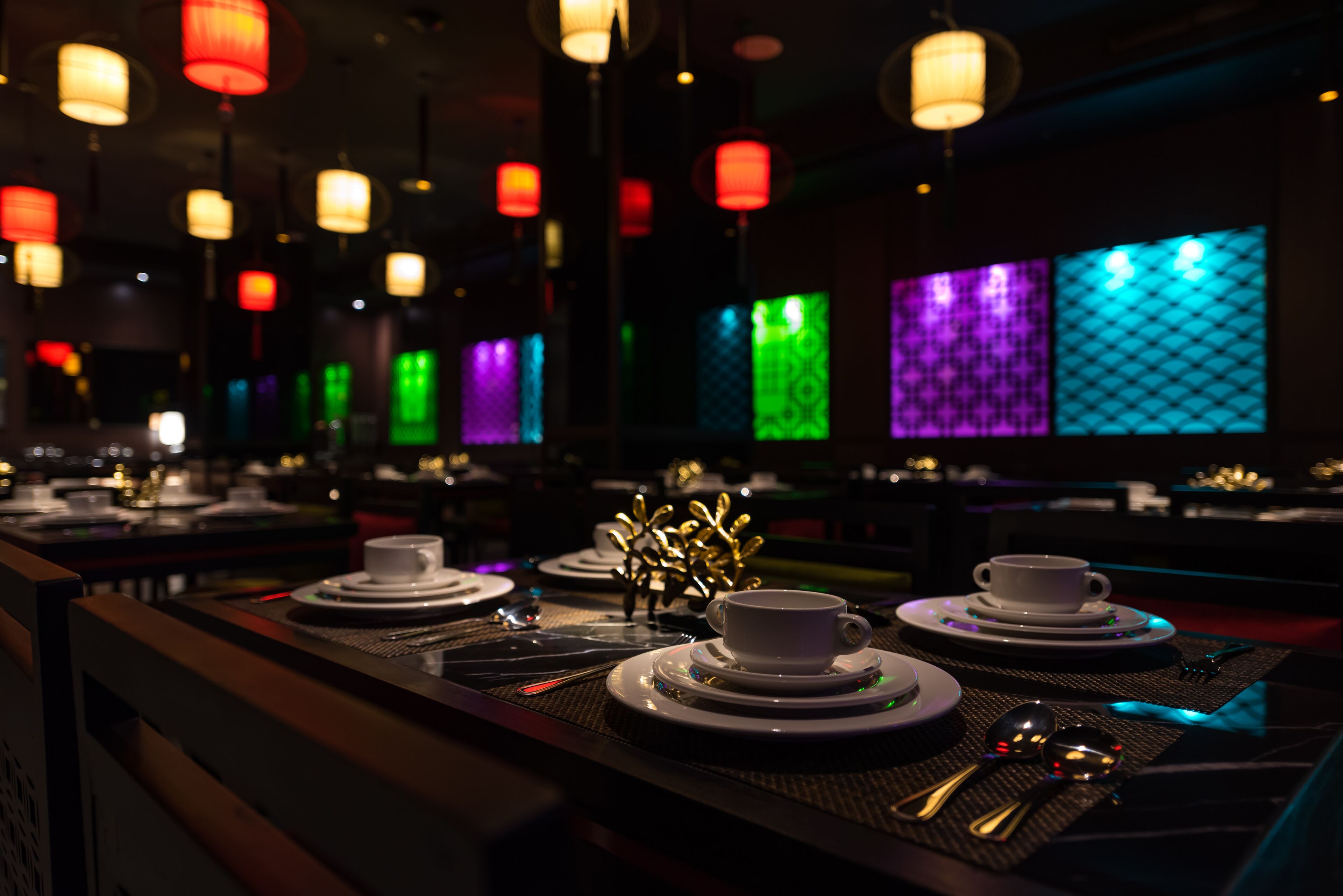 A dimly lit restaurant with tables set for dining, featuring a variety of colorful backlit panels on the walls.