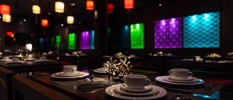 A dimly lit restaurant with tables set for dining, featuring a variety of colorful backlit panels on the walls.
