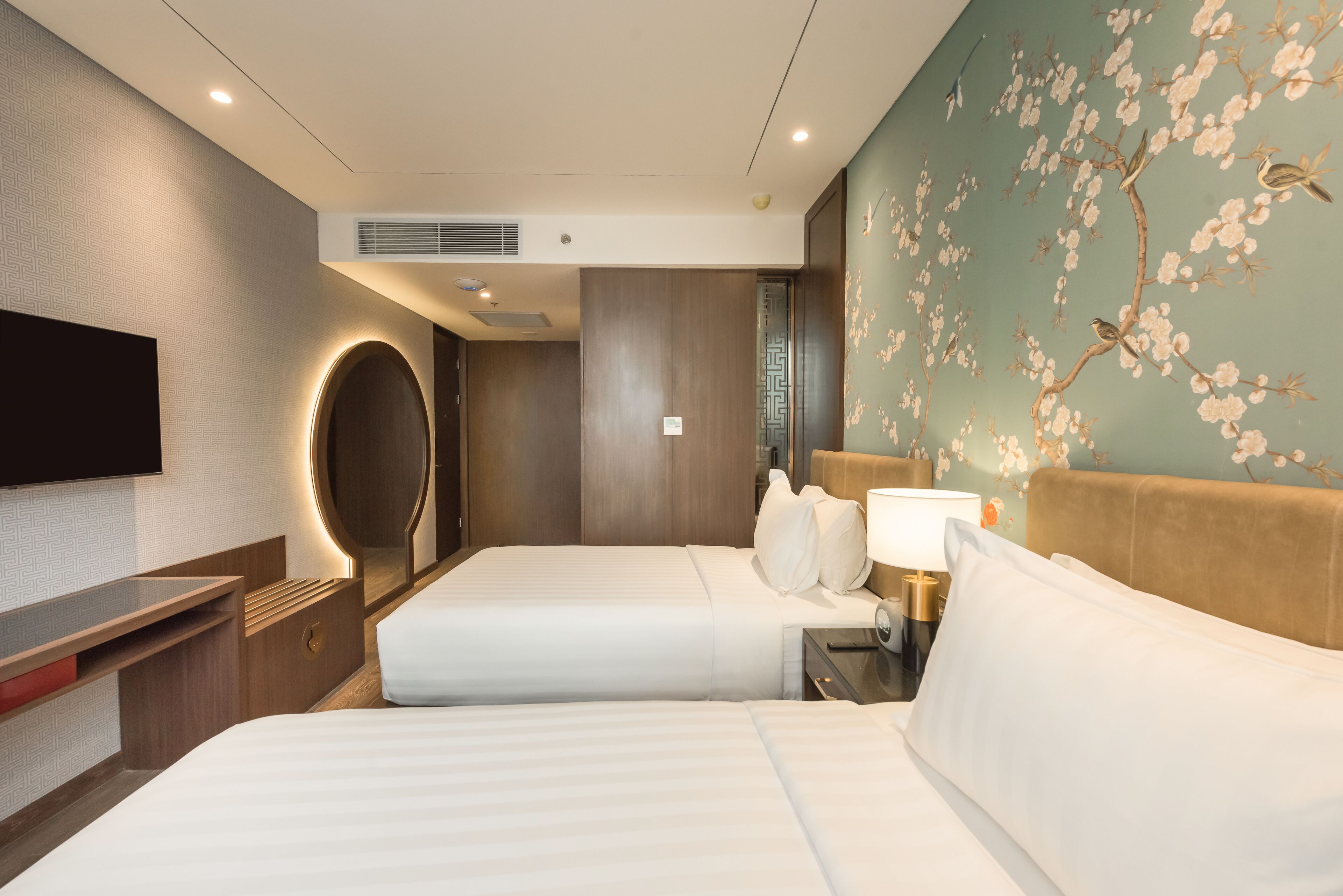 A hotel room with two beds, a TV, a wall-mounted air conditioner, and a floral mural.