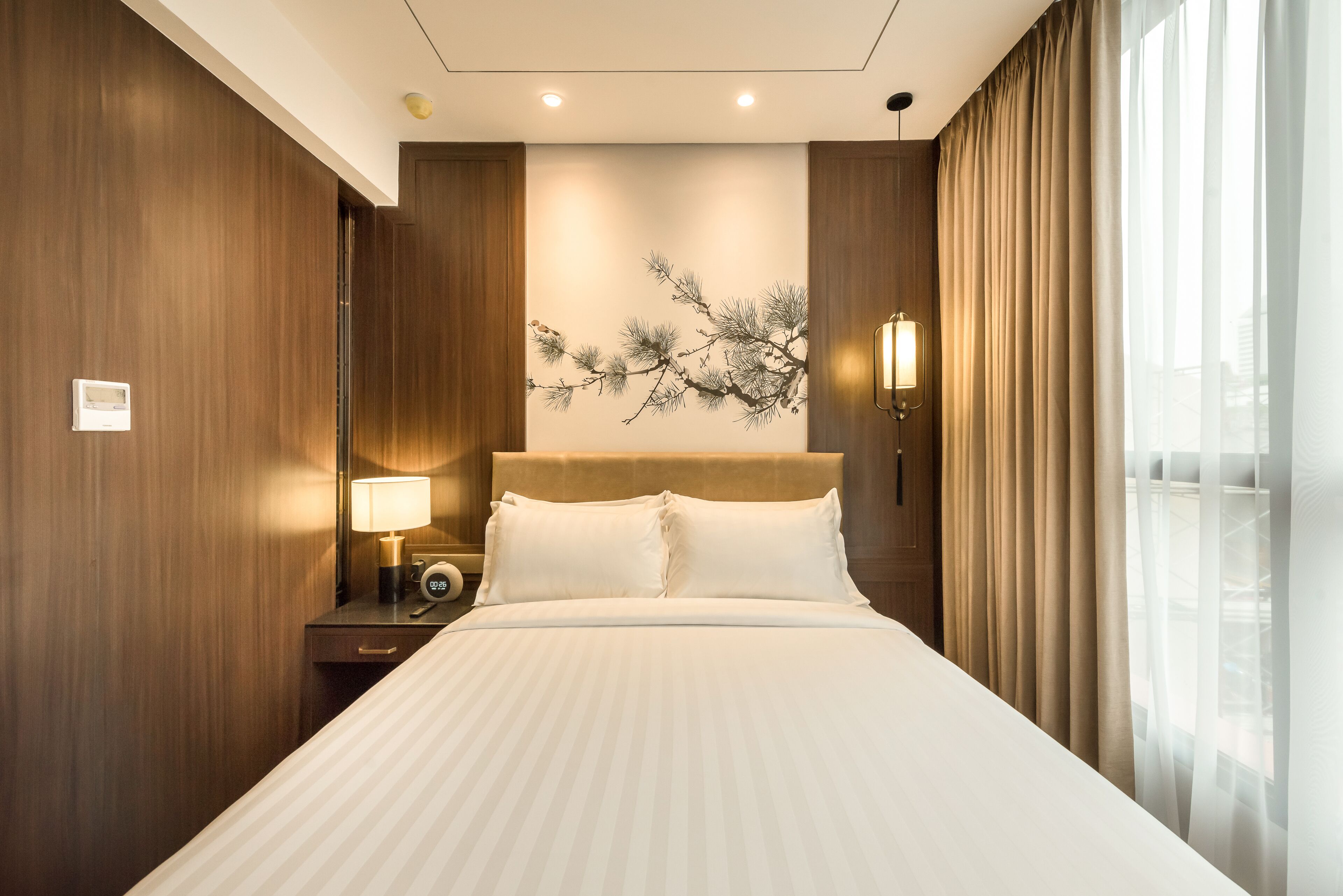 Habitación de hotel con una cama grande, paneles de madera, una obra de arte colgada en la pared, una mesita de noche con lámpara y una ventana con cortinas.