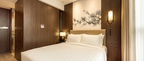 A hotel room with a large bed, wooden paneling, a wall-mounted lamp, and a nightstand with a lamp.