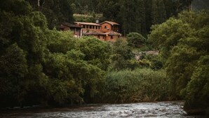 Ein rustikales Haus, umgeben von dichtem Wald, mit einem Fluss im Vordergrund.