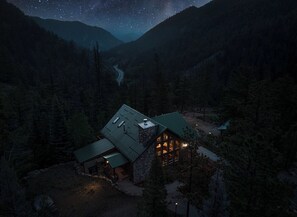 A lodge with a stone exterior and a green roof, surrounded by forested mountains under a starry night sky. - Relax, recharge and rejuvenate at Star Wrangler! (Westcliffe)
