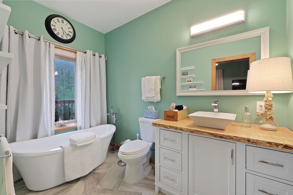 A bathroom with a bathtub, toilet, vanity with drawers, a mirror, a clock, and a window with curtains. - Relax, recharge and rejuvenate at Star Wrangler! (Westcliffe)