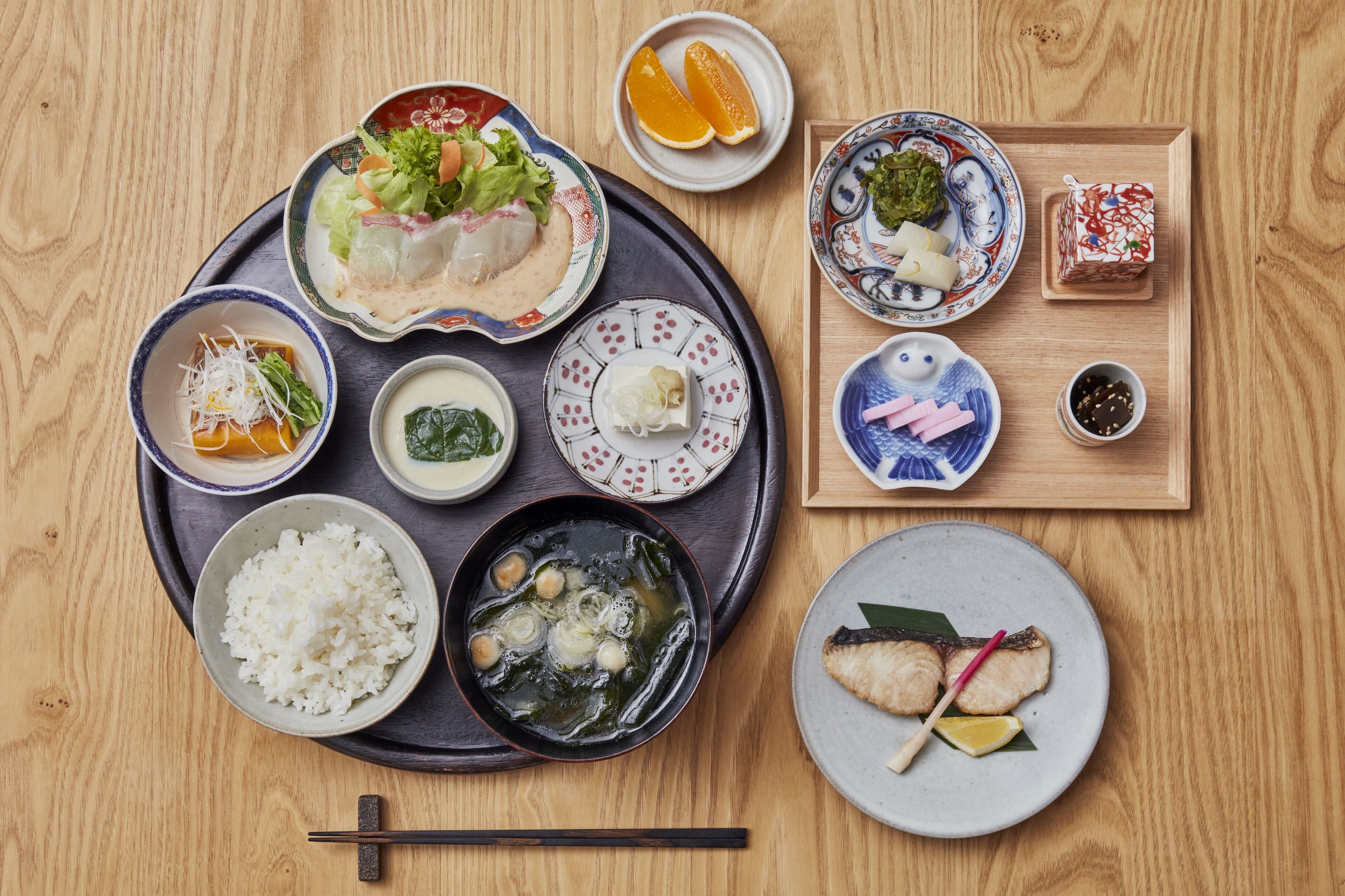 Un tavolo di legno con diversi piatti giapponesi, tra cui riso, zuppa e sashimi.