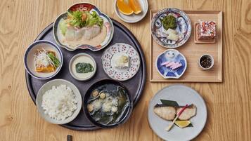 Un tavolo di legno con diversi piatti giapponesi, tra cui riso, zuppa e sashimi.