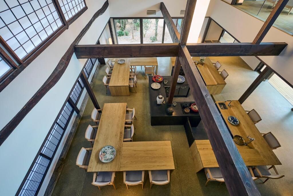 Un amplio comedor con varias mesas y sillas de madera, ventanas grandes y un techo alto con vigas a la vista.