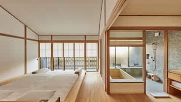 Un dormitorio de estilo japonés tradicional con suelo de tatami, una cama grande, puertas correderas shoji y vistas a un baño moderno.