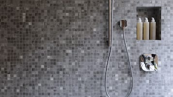 Bruser med regnbruser og håndbruser, lille hylde med toiletartikler, og flisebeklædt væg.