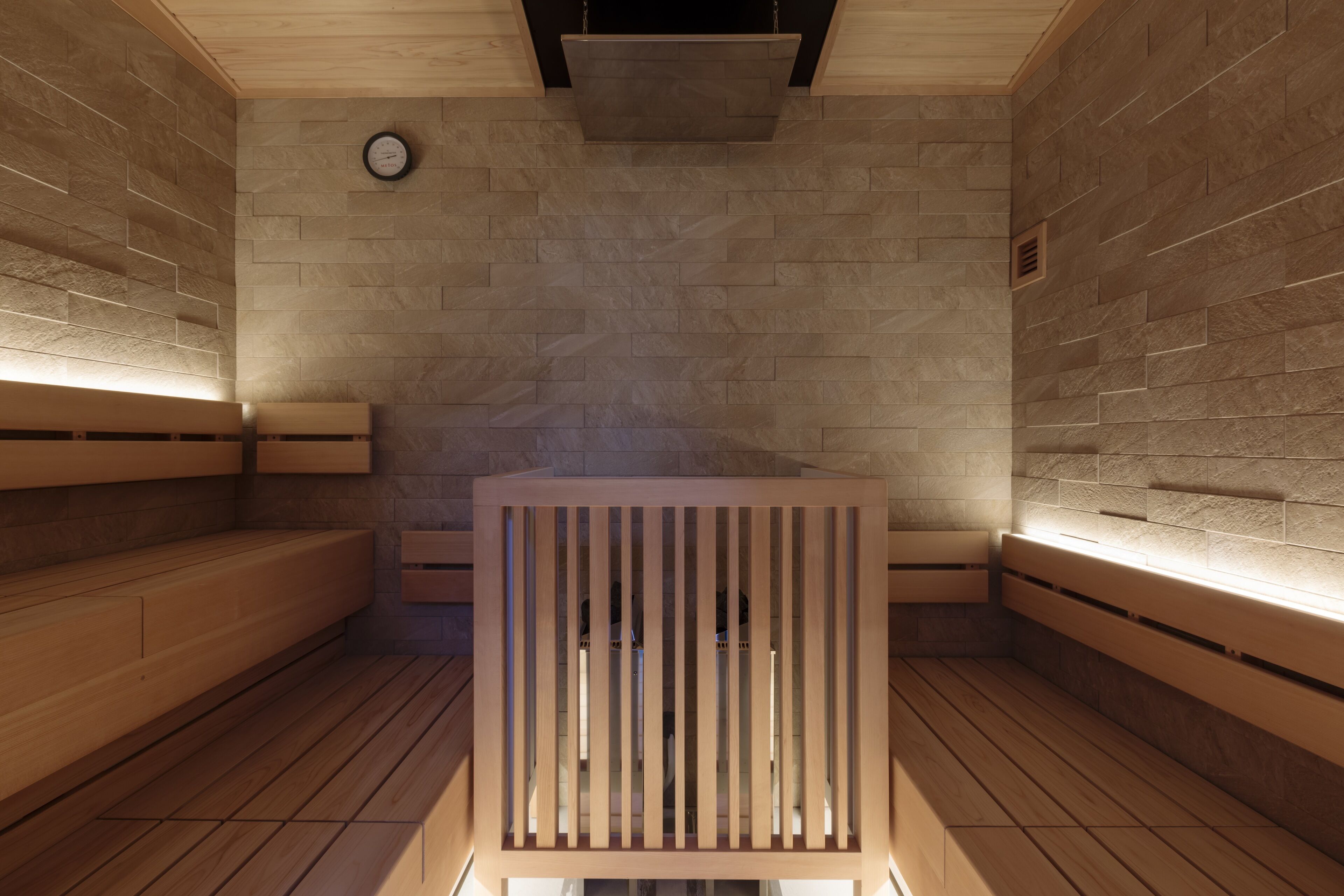Una sauna con bancos de madera, un muro de piedra y un reloj en la pared.