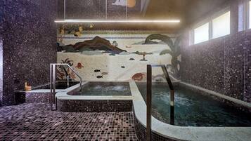 Ein Wellnessbereich mit Mosaikwand, Whirlpool und einer kleinen Wasserfallanlage.