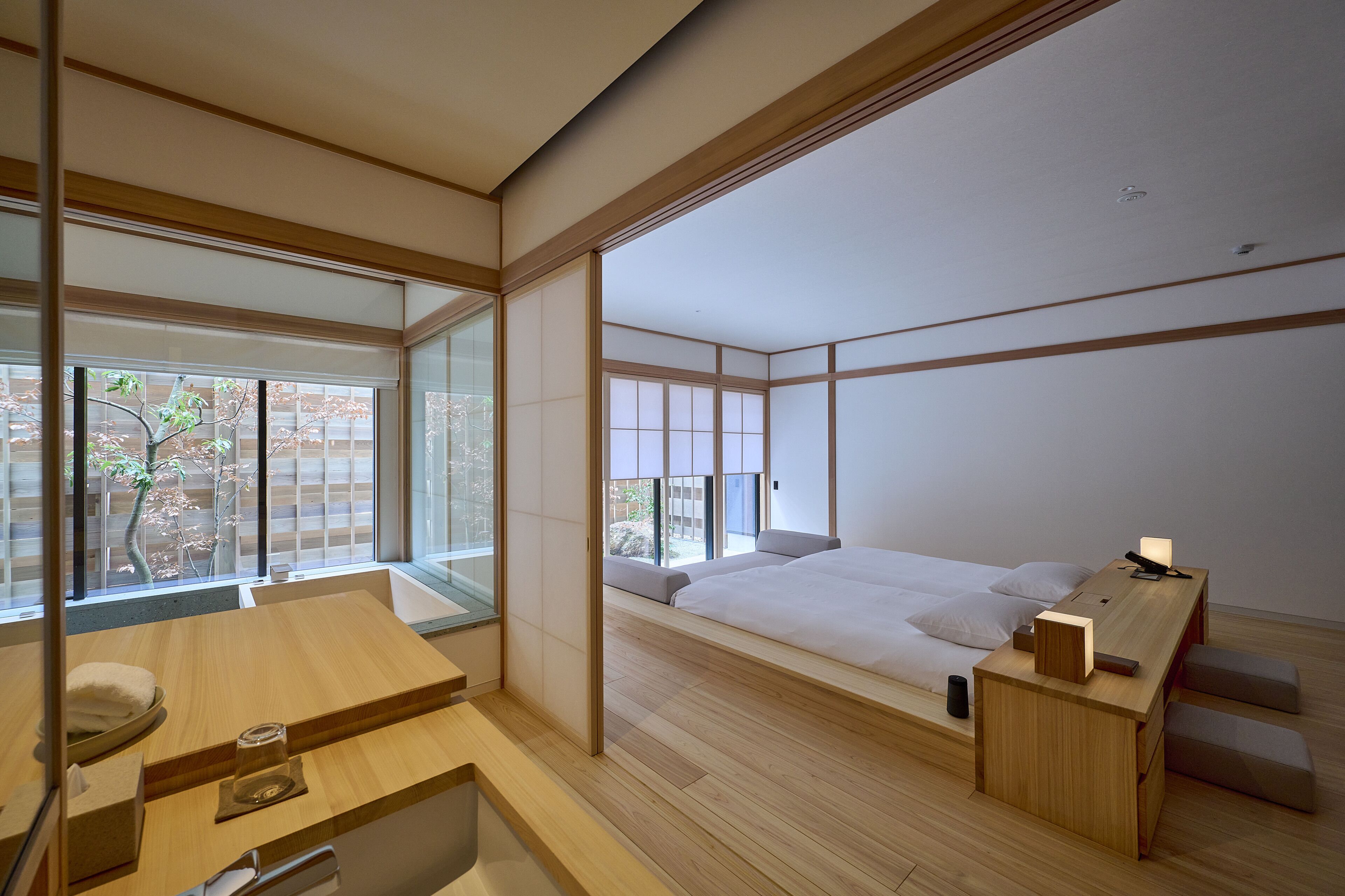 Un dormitorio minimalista con cama de madera, mesitas de noche y un ventanal con vistas a árboles.