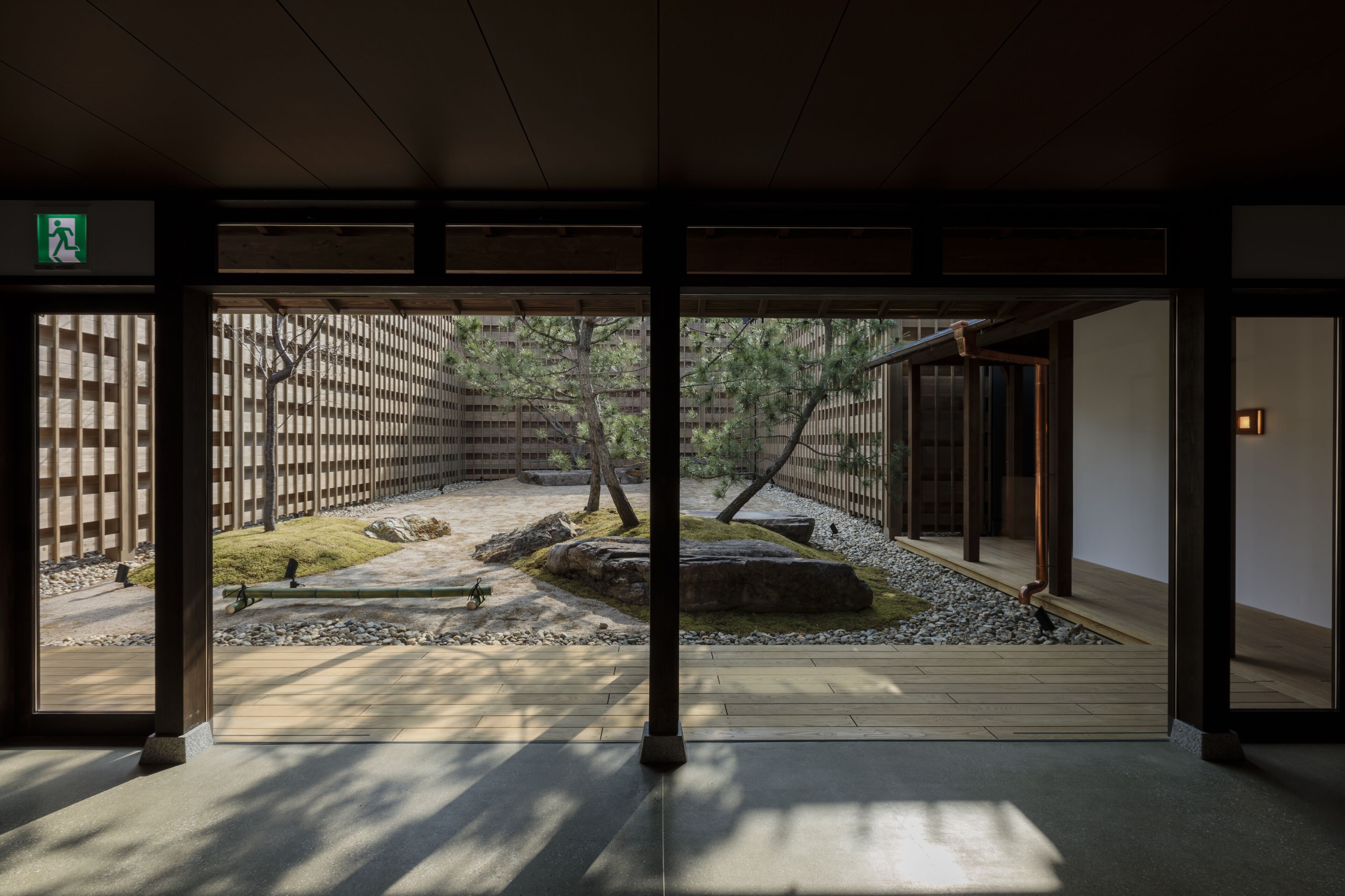 Un interior japonés tradicional con suelo de tatami, vigas de madera y vistas a un jardín exterior con rocas y árboles.