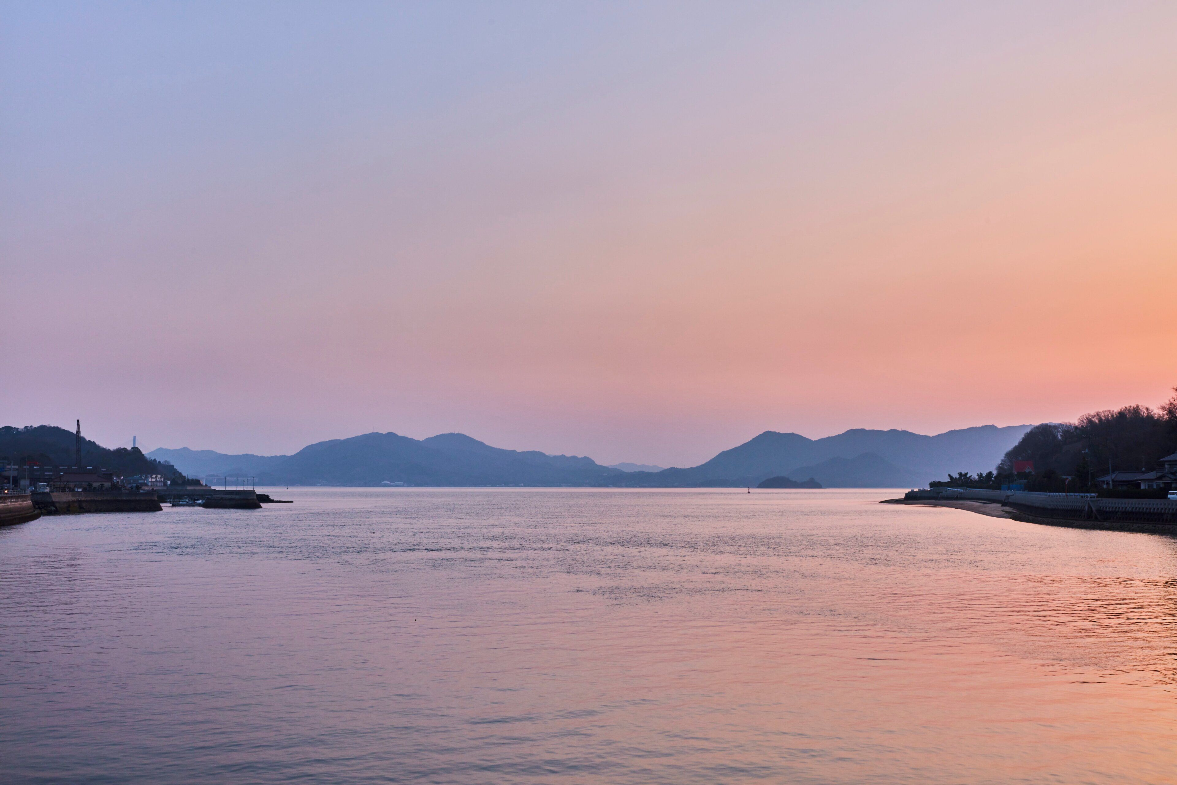 A calm river at sunset with distant mountains and a small town on the banks.