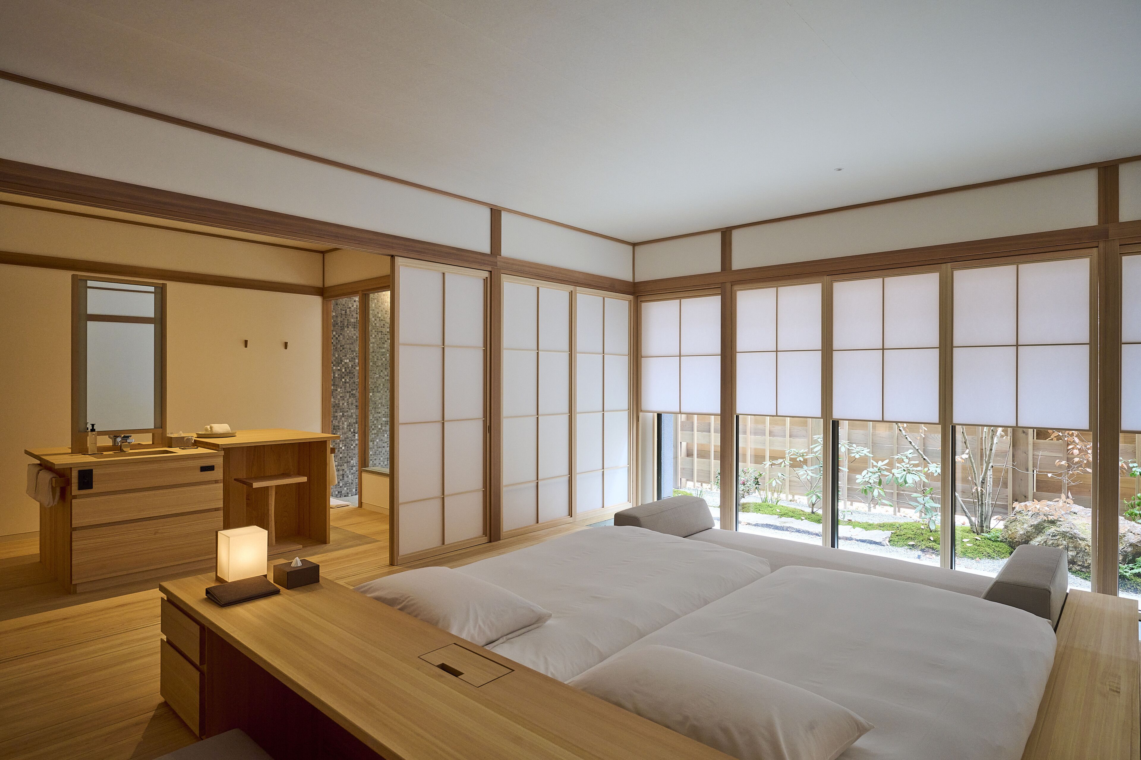 A traditional Japanese-style bedroom with tatami flooring, a wooden desk, a bed with white bedding, and large shoji screens.