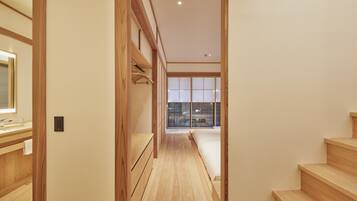 A narrow hallway with wooden flooring and walls, leading to a staircase and a room with a large window.