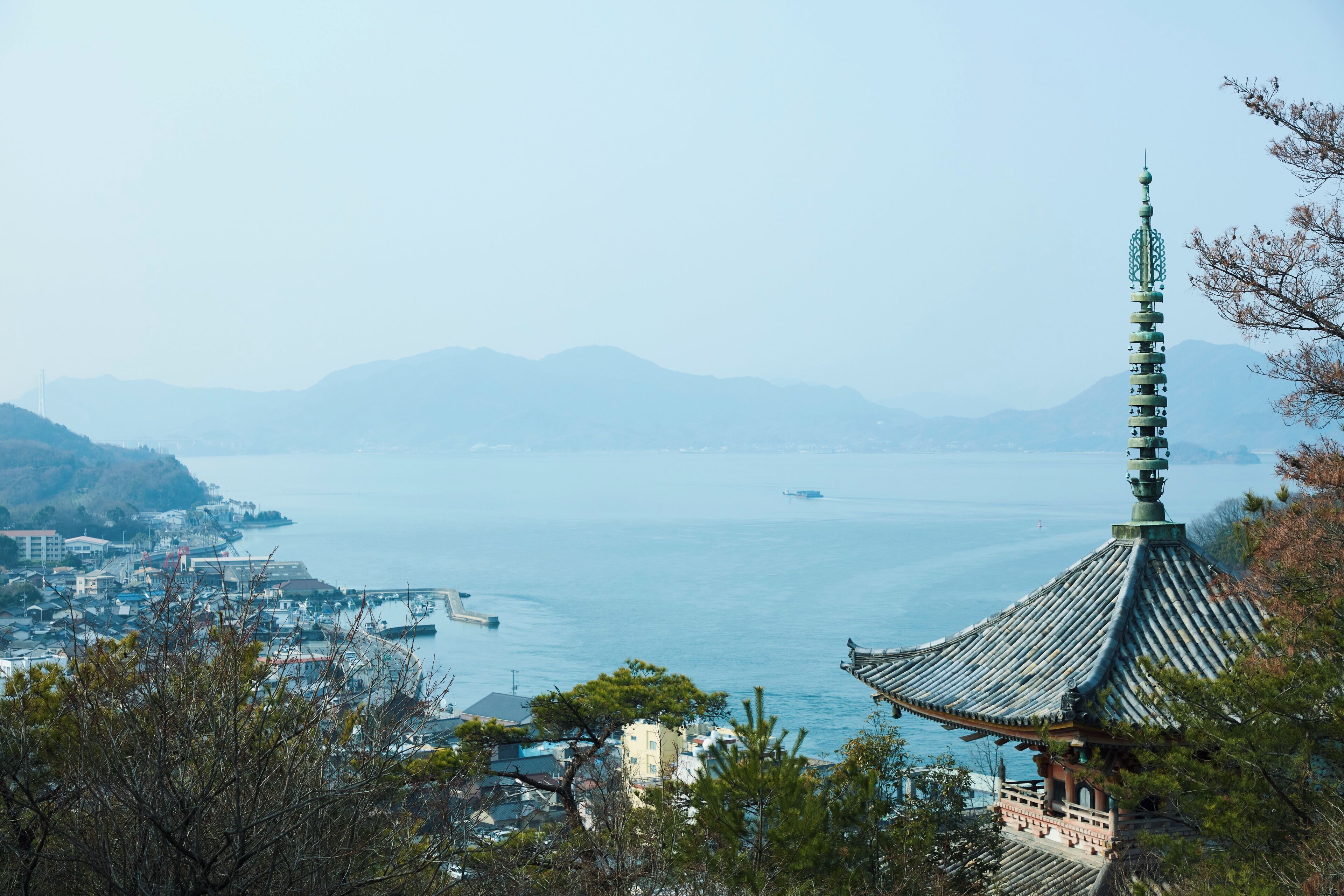 A coastal view with a traditional pagoda and a distant cityscape.