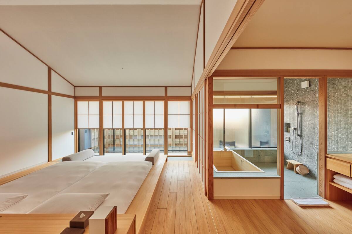 A traditional Japanese-style bedroom with tatami flooring, a large bed, sliding shoji doors, and a view of a modern bathroom.