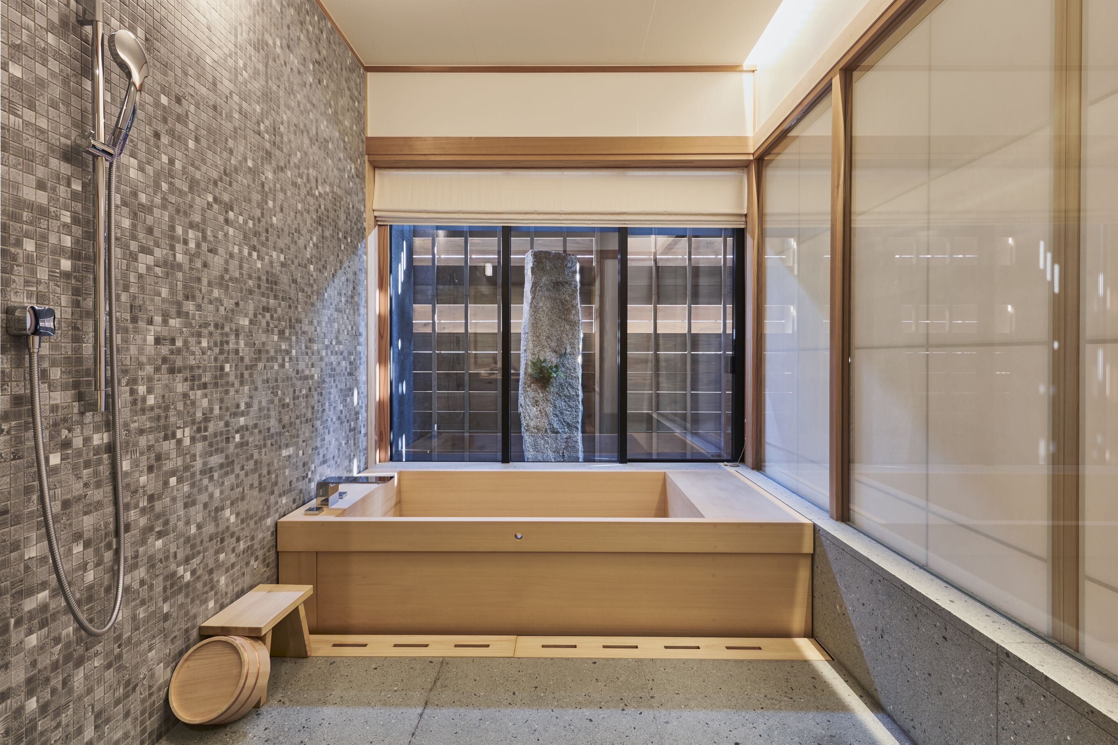 A modern bathroom with a large bathtub, a shower, and a wooden bench.