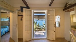 Ein Zimmer mit Holzboden, Blick auf das Meer durch eine offene Tür und einem Bett mit gestreifter Bettwäsche.