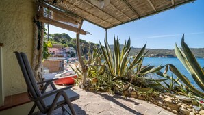 Eine überdachte Terrasse mit Steinboden, einem Stuhl und verschiedenen Pflanzen.