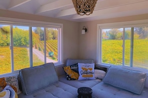 Quarto com uma grande janela e vista para um vinhedo, sofá com almofadas e um travesseiro decorativo.