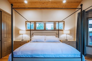 Uma cama de dossel com cabeceira, duas mesas de cabeceira e uma janela com cortinas.