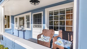 A porch with wicker chairs, a white railing, and a window with a view of a house. - Charming Dog-Friendly Cottage Near Beach (Capitola)