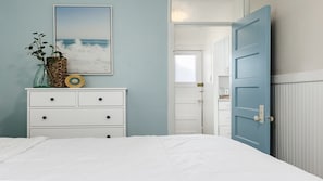 A bedroom with a bed, a dresser, a wall-mounted picture, and an open door leading to another room. - Charming Dog-Friendly Cottage Near Beach (Capitola)