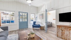 A spacious living room with a blue door, a blue armchair, a wooden coffee table, and a television. - Charming Dog-Friendly Cottage Near Beach (Capitola)