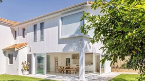 Ein modernes, zweistöckiges Haus mit Terrasse, Essbereich und Einblick in eine Küche durch Glastüren.