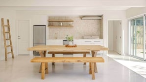 A modern kitchen with white cabinetry, a wooden dining table with benches, a refrigerator, and a window providing a view of the outdoors. - Torretta by the Bay (Dunsborough)