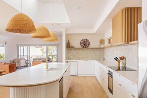 A modern kitchen with a central island, pendant lights, a clock, and a view to the living area.