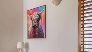 Ein modernes Wohnzimmer mit einem grauen Sofa, einem farbenfrohen Gemälde, einer Lampe und einem Fenster mit Jalousien.