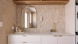 Ein Badezimmer mit weißem Waschtisch, goldenem Wasserhahn, einem Spiegel mit Bogenform und einer gefliesten Rückwand.